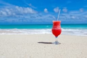 Picture of a cold tropical drink on a beach by the ocean representing a vacation which can be purchased by refinancing a mortgage
