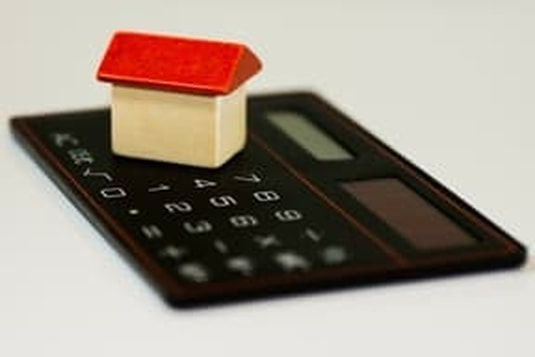 Picture of a mortgage calculator with a toy house on top of it representing the calculation of a mortgage refinance contract